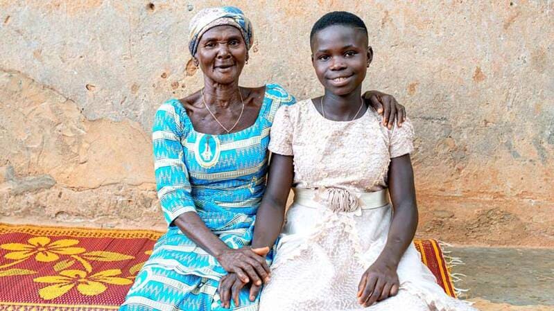 A woman embraces Anne (a young girl) and both smile at the camera A woman embraces Anne (a young girl) and both smile at the camera