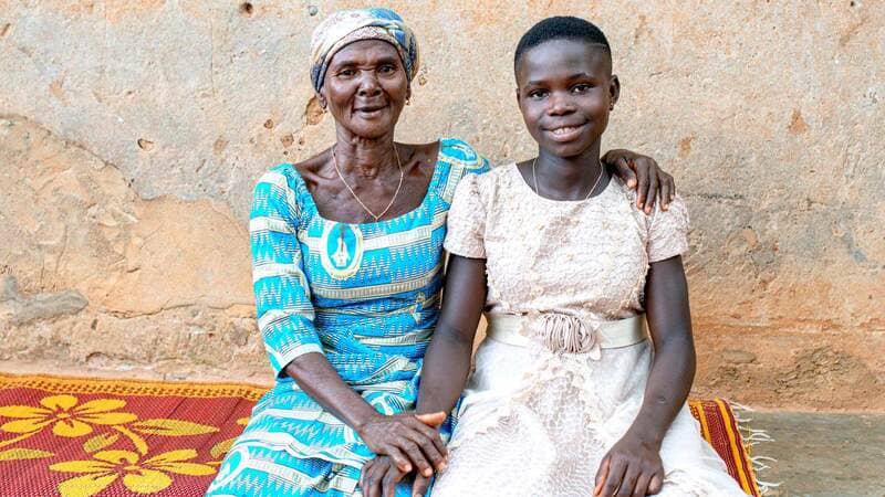 A woman embraces a young girl and both smile at the camera.