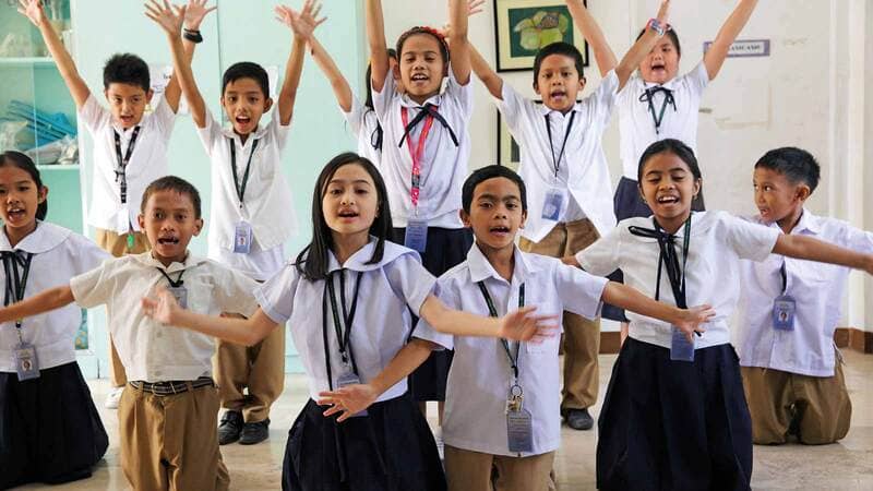 A group of children in uniforms raise their hands.