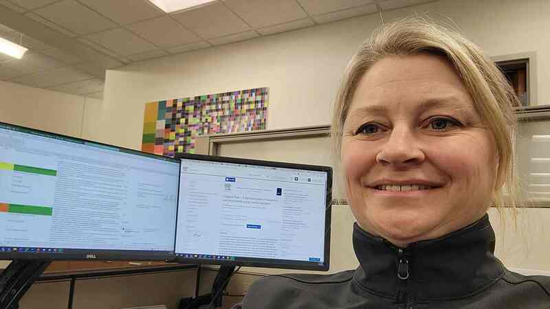 A woman smiles while sitting in front of a computer screen with a food science article on it.