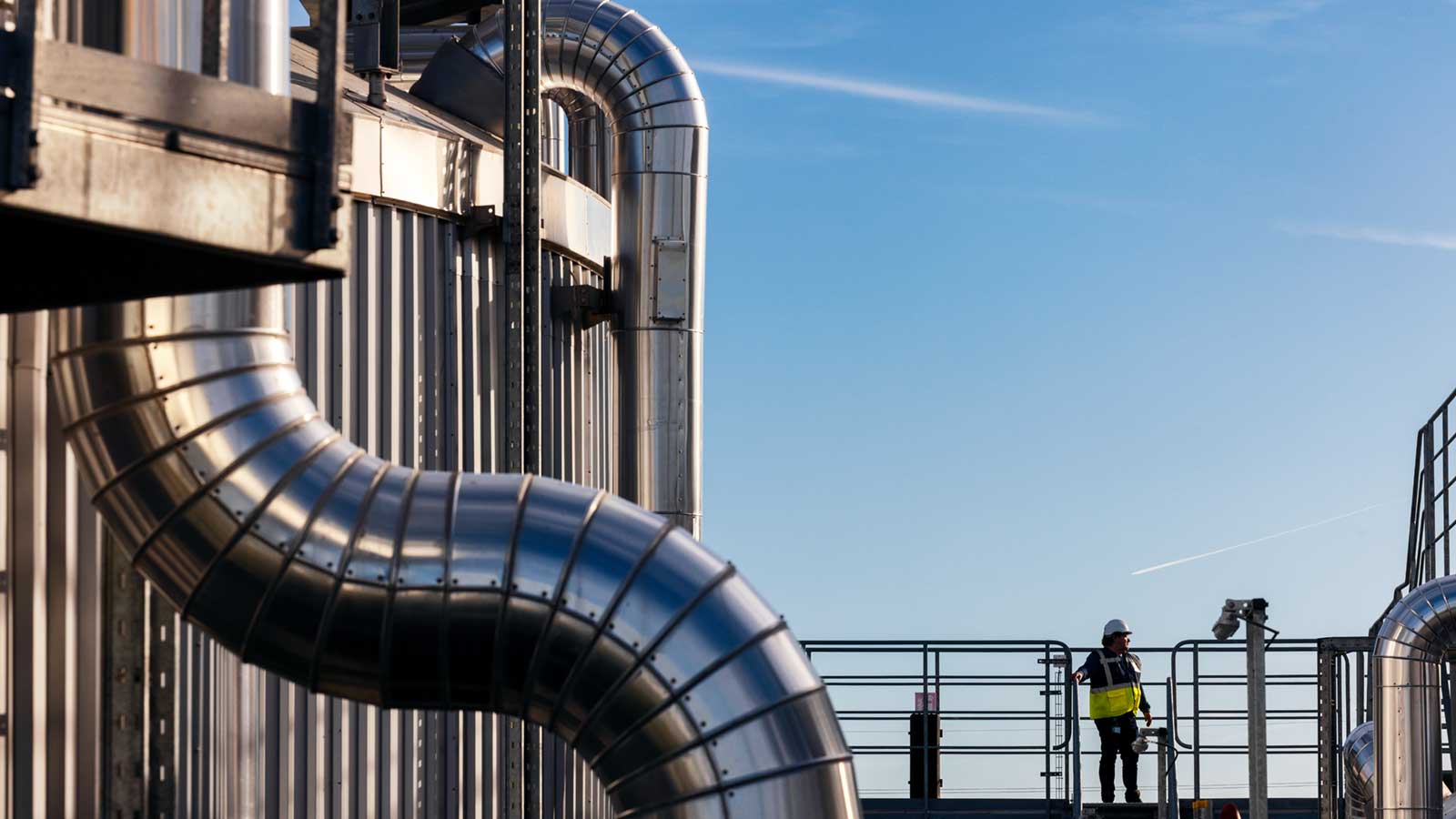 A worker wearing a hard hat and glasses looks out over a plant that makes bioenergy and biofuel.  A worker wearing a hard hat and glasses looks out over a plant that makes bioenergy and biofuel.