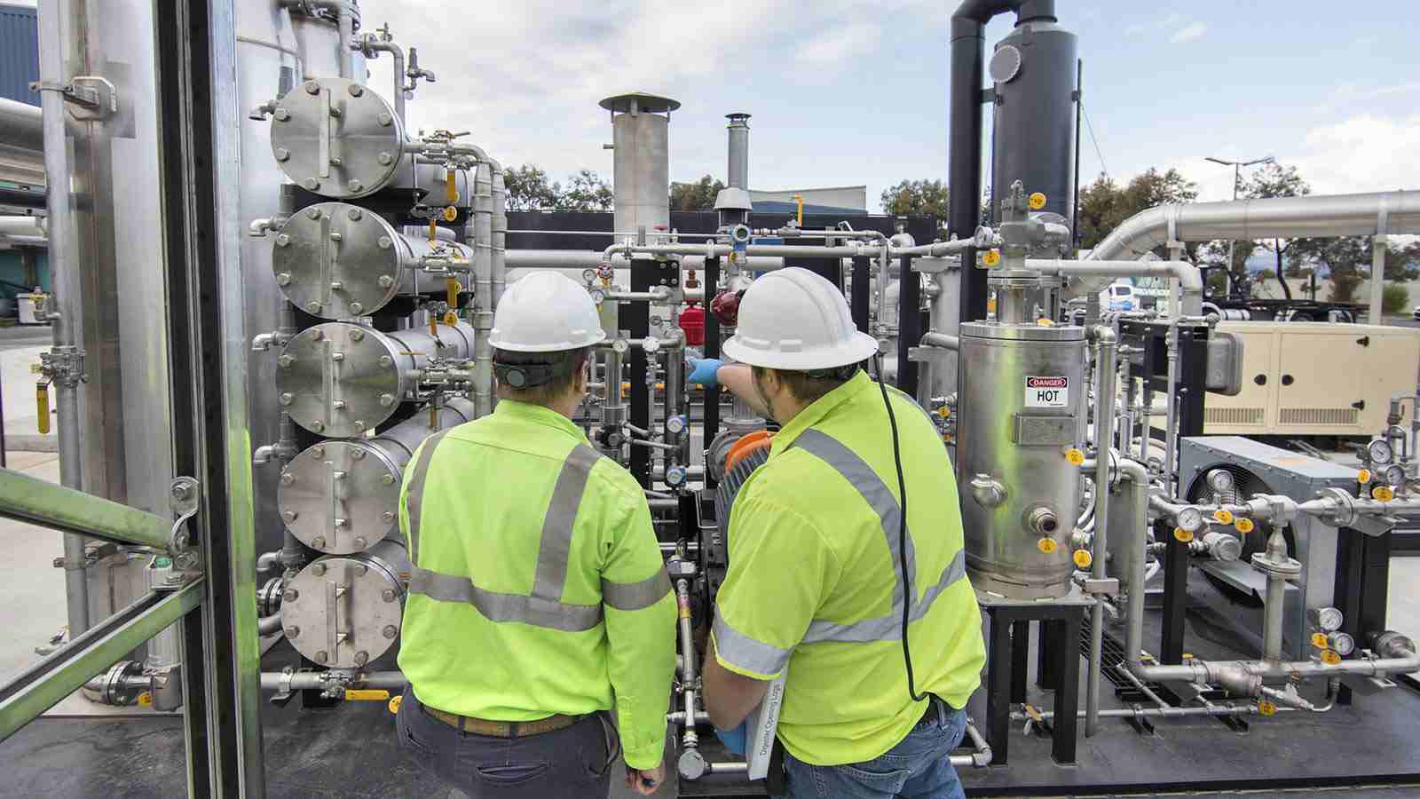 Two men point to a machine producing biogas.  Two men point to a machine producing biogas.