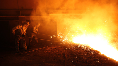 A person in a protective suit works with a blue flame on a piece of metal. A person in a protective suit works with a blue flame on a piece of metal.