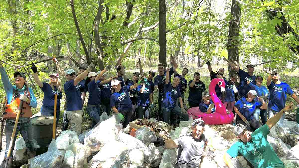 A large group of people surrounded by trees smile next to dozens of bags of recently removed trash.   A large group of people surrounded by trees smile next to dozens of bags of recently removed trash.