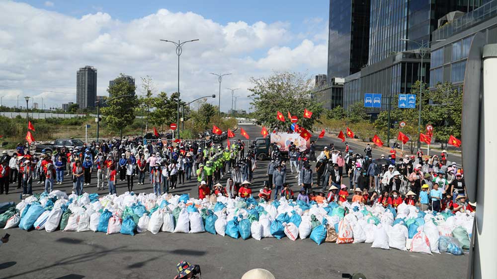 A large group of people with Vietnam flags pose next to hundreds of trash bags. 