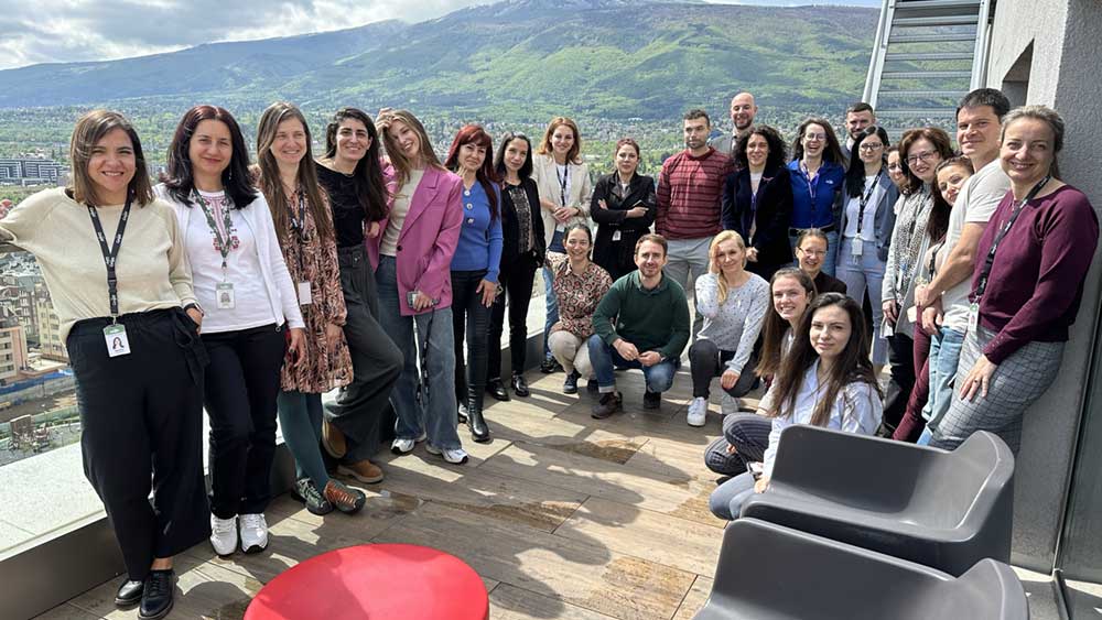 A group of employees pose for the camera at an office setting, with mountains in the background.   A group of employees pose for the camera at an office setting, with mountains in the background.