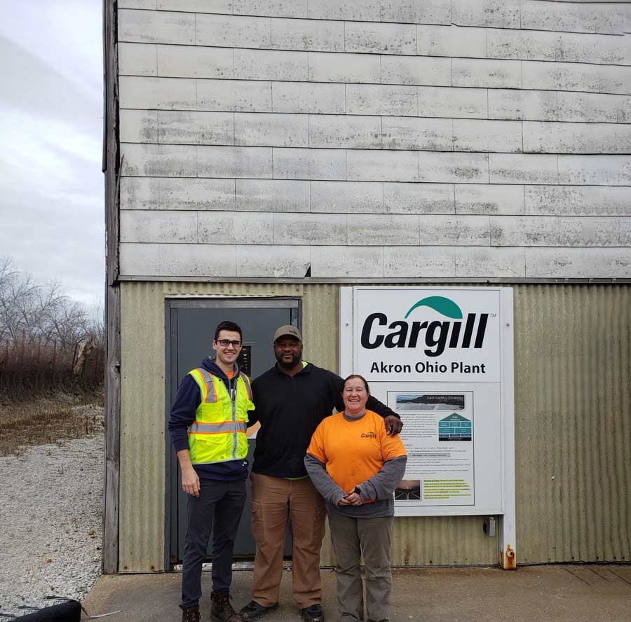 Three plant employees standing in front of a salt facility. 