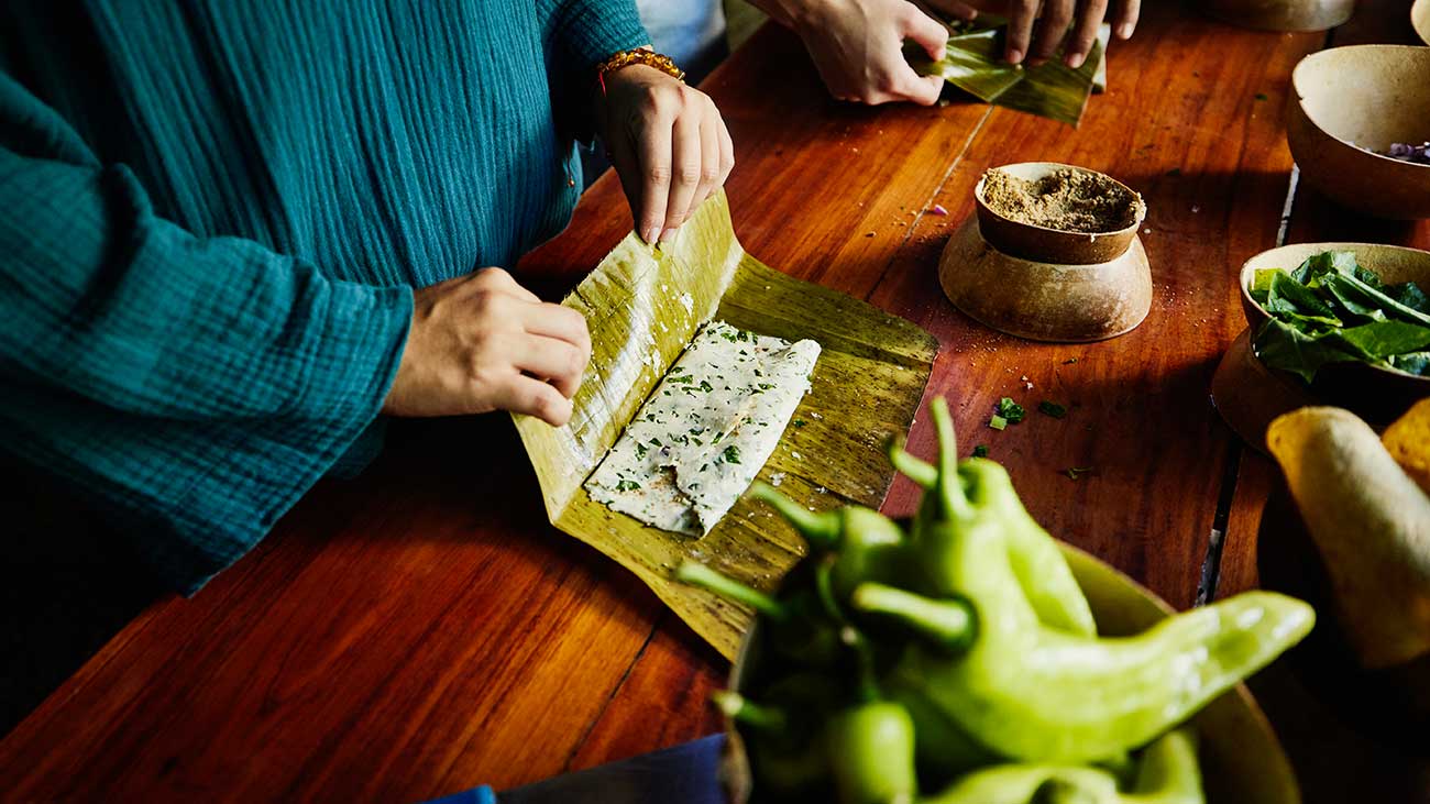 A person wraps up a tamale on a large cooking table. 