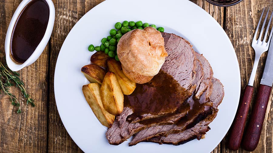 Steak, potatoes, peas and a biscuit on a plate. 