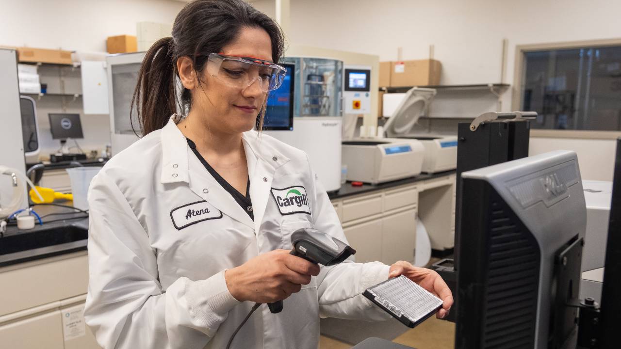 A Cargill crop innovation scientist scans a small tray of plant simples while standing in front of a computer. 