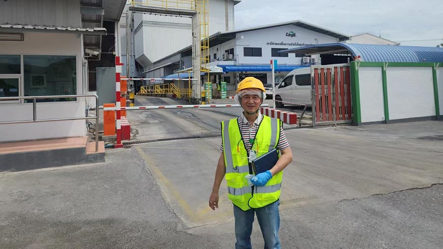 A man wearing a yellow hard hat and yellow safety vest stands outside an operations facility.  A man wearing a yellow hard hat and yellow safety vest stands outside an operations facility.