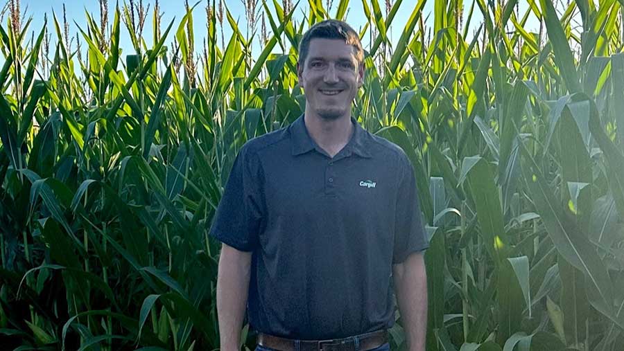 A man wearing a gray shirt with a Cargill logo stands in front of a row of corn. 