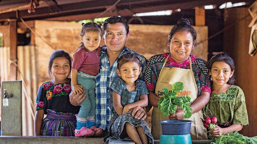 A woman and man stand with four children and hold vegetables in their hands.  A woman and man stand with four children and hold vegetables in their hands.