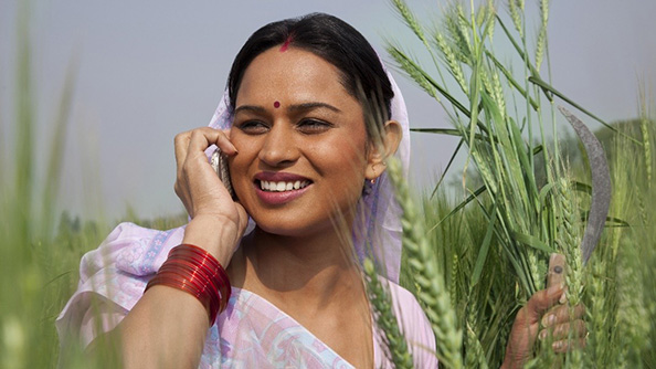 A woman standing next to a wheat field speaks into a cell phone.  A woman standing next to a wheat field speaks into a cell phone.